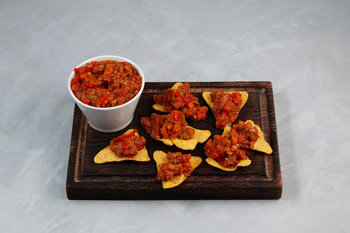 Chili con carne with tortilla corn chips on brown wooden cutting board. Tex-mex food. Traditional Mexican spicy dish with red beans, peppers, tomatoes and minced meat.