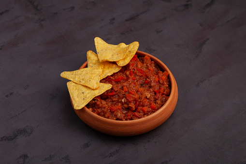 Chili con carne in clay plate with tortilla chips on brown background. Traditional dish of mexican cuisine.