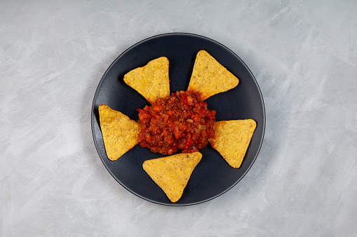 Chili con carne with tortilla corn chips on dark plate, top view. Traditional Mexican food, spicy dish with red beans, peppers, tomatoes and minced meat.