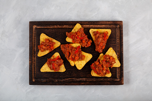 Delicious spicy Chili con carne with tortilla corn chips on wooden board, top view. Mexican spicy dish with red beans, peppers, tomatoes and minced meat.