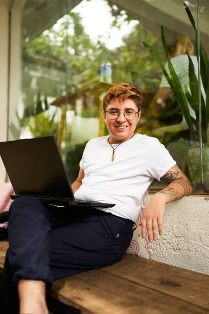 istock Transgender pro smiles while working on laptop in casual office space. Relaxed attire, inclusive work environment evident. Barefoot, shows comfort, tech engagement and confidence. 2151725629