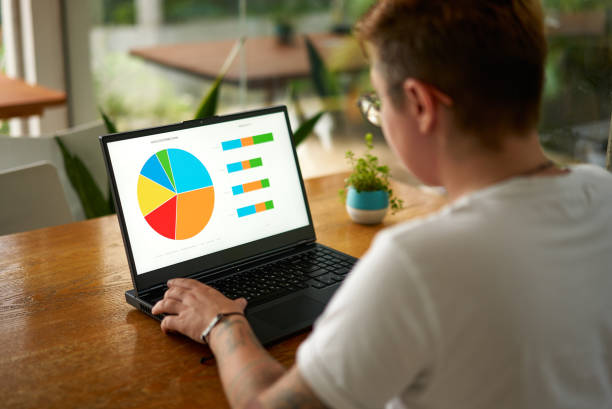 istock Transgender office worker analyzes data charts on laptop screen in bright workspace. Pro with tattoo interacts with business analytics report. Inclusive workplace, modern employee engaged in market. 2151725921