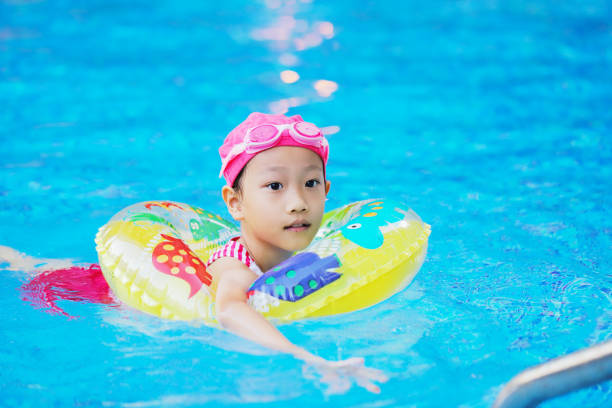 Asian girl playing with water in swimming pool while practicing how to swim. she wore swimming rings, goggles and sleeves to prevent them from sinking into the water