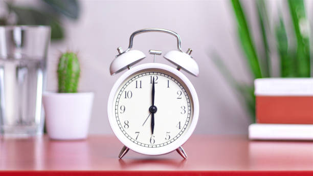 istock Classic white clock on a table. The clock hand points at 6:00. close up 2151731523