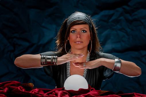 Fortune teller with Cristal ball on red velvet. Looking at camera.