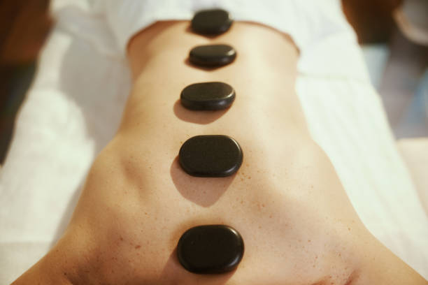 Healthcare time. Closeup on relaxed woman in massage cabinet having hot stone massage and laying on massage table.