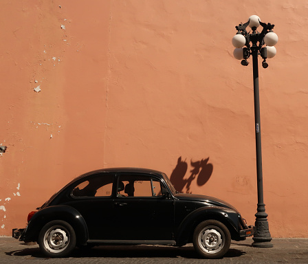 Vintage black car parked next to a street lamp in front of a orange wall in Puebla, Mexico 2022