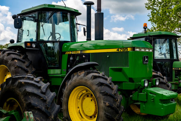 A tractor is sitting on a field of grass. The sky is clear and blue, with a few clouds scattered throughout. The scene is peaceful and serene
