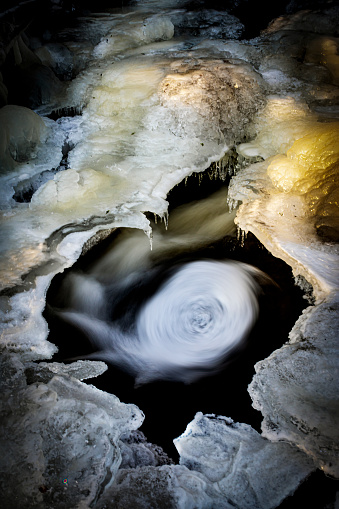 Winter wonderland with icy surrounding by a flowing creek, cirkular mystical pattern in the pond, long exposure