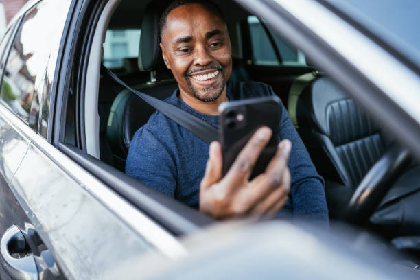 Mature black man driving car and using smart phone