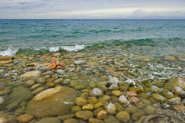 Northern Kyrgyzstan. The landscape of the cold Issyk-Kul lake with colored rounded stones of various sizes along the picturesque shore.