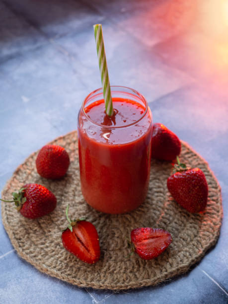 A glass of homemade strawberry smoothie with a straw on a blue table