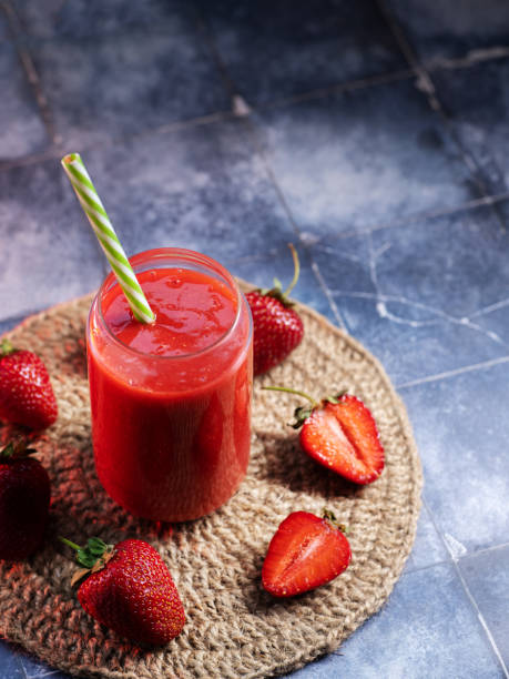 A glass of homemade strawberry smoothie with a straw on a blue table, copy space