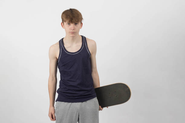 A fifteen year old skater boy holding a skateboard against a white background