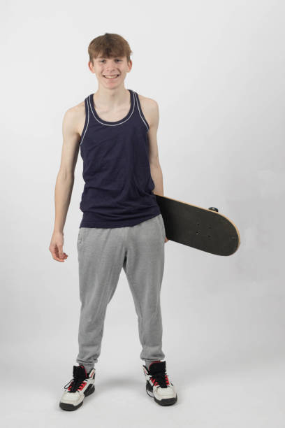 A fifteen year old skater boy holding a skateboard against a white background