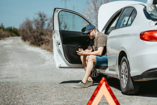 istock Broken car on a road. Man calls roadside assistance and asking for help. Red warning triangle set up near the motorway 2151761642