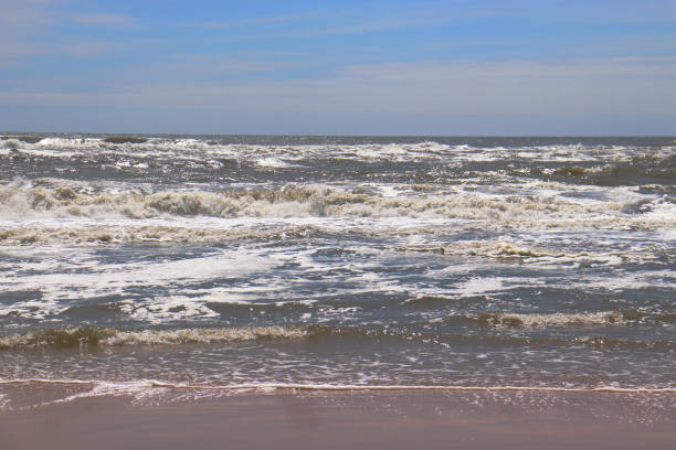 Southhampton New York beach with small frothy waves crashing onto beach on a partly cloudy blue-sky day