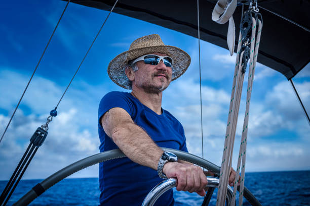 A man wearing a straw hat is driving a sailboat and enjoying it.