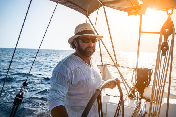A man wearing a straw hat is driving a sailboat and enjoying it.