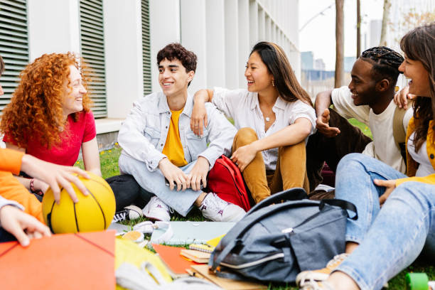 istock High school student friends hanging out at campus grass. 2151777231