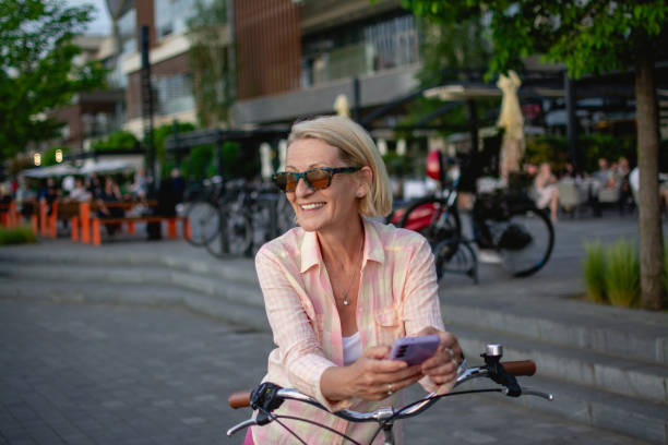 istock mature blonde woman on mobile phone while in town with bicycle 2151780574