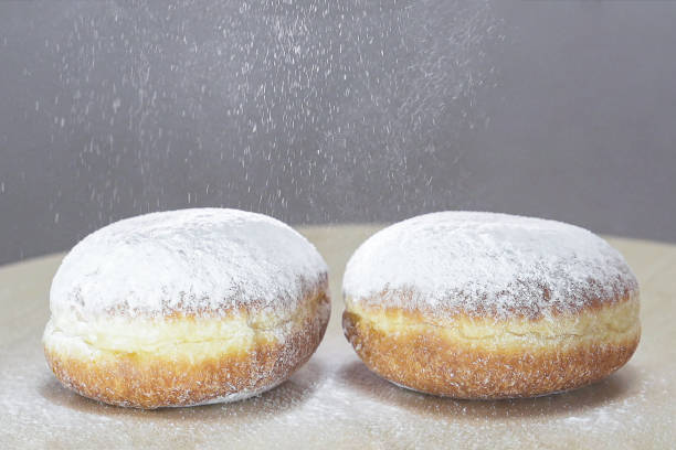 Doughnuts, Sugar powder is being delicately sprinkled onto Hanukkah doughnuts, creating a festive culinary process.