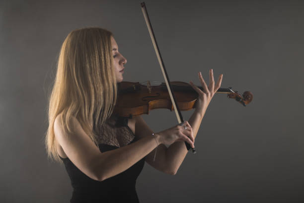 istock Elegant young woman playing violin in a moody studio setting 2151785456
