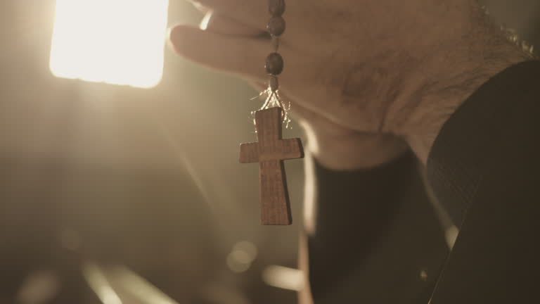 Christian rosary with cross hanging from male hands up
