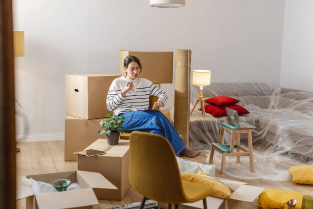 istock Young woman talking on the phone and holding documents while packing for moving 2151791055