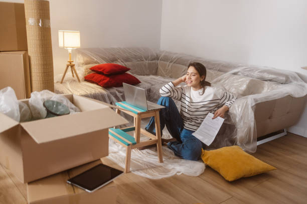 istock Young woman using laptop in new home and holding documents 2151791468