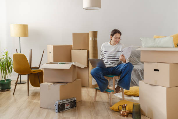 istock Young woman using laptop in new home and holding documents 2151791795