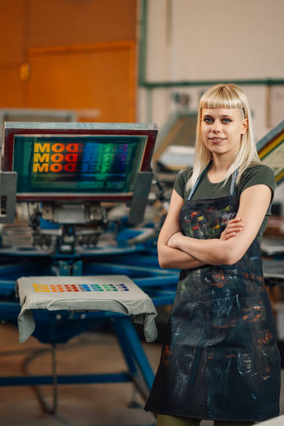 istock Entrepreneur near silkscreen printing press smiling at the camera. 2151795782