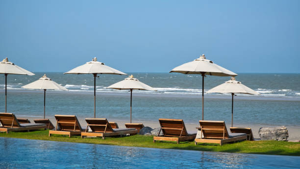 Beachfront resort with poolside, lounge chairs and white parasol on sunny day