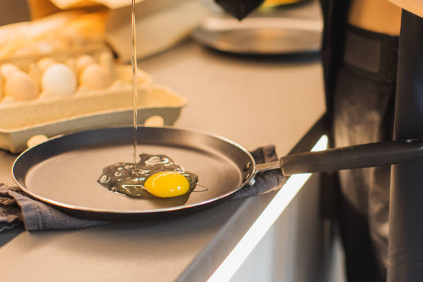 Woman breaks eggs into frying pan.