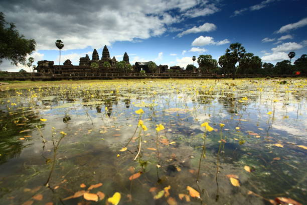 Angkor Wat, Cambodia – September 1, 2019: A faint rainbow appears in the sky above Angkor Wat temple, beautifully mirrored in the still water of a pond in the foreground. Palm trees and the iconic temple towers are reflected, creating a serene scene after rainfall.