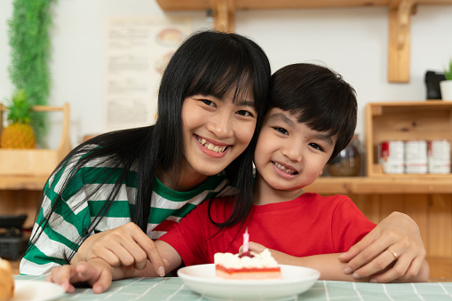 Asian mother celebrates her son's birthday with cupcakes in the kitchen. The family's happiness on a relaxing day at home during the weekend.