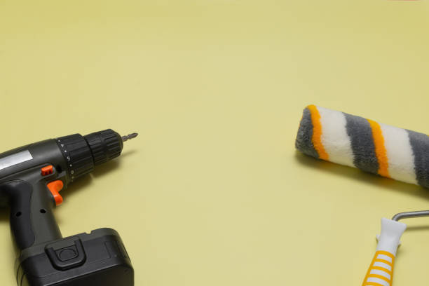 istock Electric screwdriver and paint roller on a yellow background. Construction tools for repair. Flat layout. There is space for text 2151832676