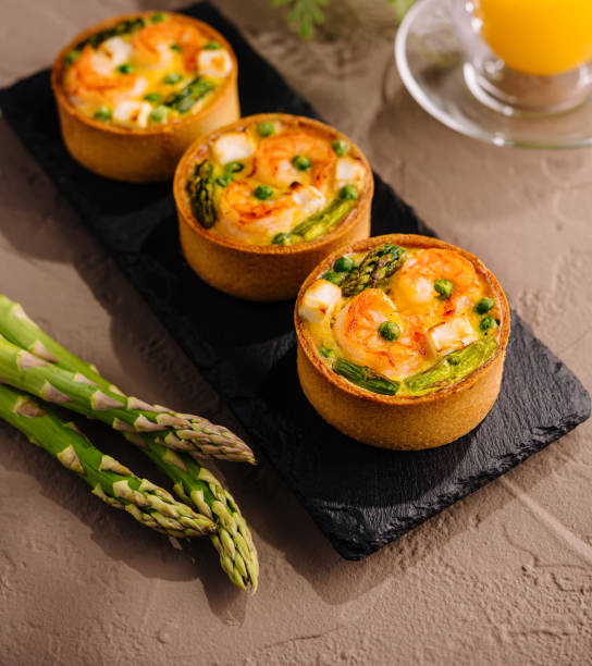 Gourmet mini quiches with fresh asparagus on a slate plate, paired with orange juice and fern decoration
