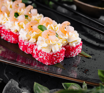 Exquisite sushi rolls topped with shrimp, caviar, and creamy sauce on a sleek black plate