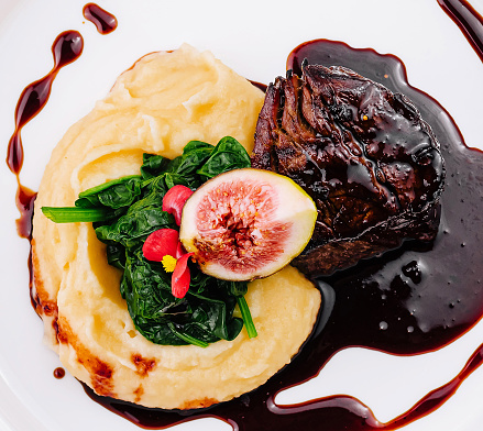 Exquisite plate of beef tenderloin with a slice of fig, spinach, and creamy mashed potatoes drizzled with reduction sauce