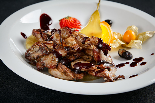 Gourmet teriyaki chicken wings paired with vibrant fruits on a textured black table. A symphony of taste and elegance in culinary presentation.