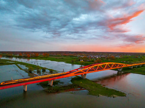 Hanzeboog train bridge over the river IJssel with a train passing over the red bridge near the city of Zwolle in Overijssel, The Netherlands. Aerial drone point of view.Amazing colorful sunset over the river IJssel in Overijssel, Netherlands during springtime seen from above. The strong colors in the sky are partly caused by the southern wind bringin sand from the Sahara desert over the European contintent.