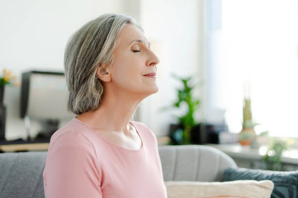 istock Smiling active senior woman sitting with closed eyes on comfortable sofa relaxing at home 2151852966