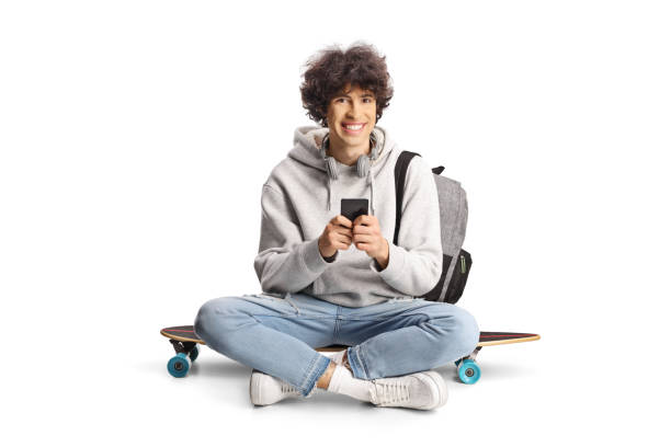 istock Male student with a backpack sitting on a skateboard and typing on a smartphone 2151855641