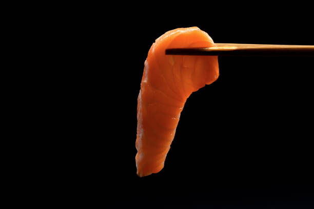 Closeup chopsticks with fresh salmon sashimi against black background.