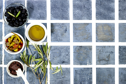 Tapenade - paste made from olives. Bowls with spreadable black and green olive cream and oil on tiles background