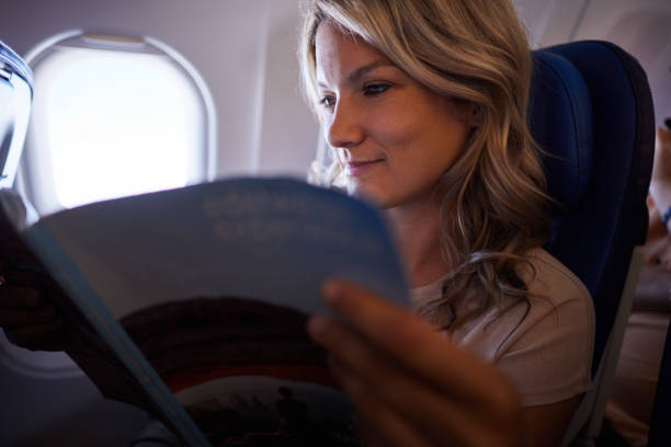istock Smiling woman reading a magazine in a plane. 2151864383