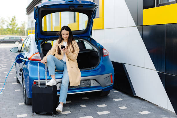 istock Young woman waiting charging automobile battery from small public station and using smartphone while charging automobile 2151867968