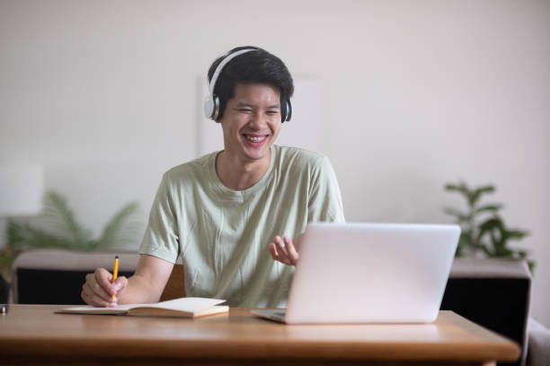istock Young Asian student doing homework and studying online, online video call on laptop happily at home 2151869422