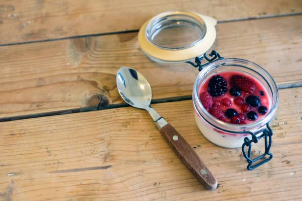 Yogurt or pudding with fresh various berry fruits in a jar on a wooden table.